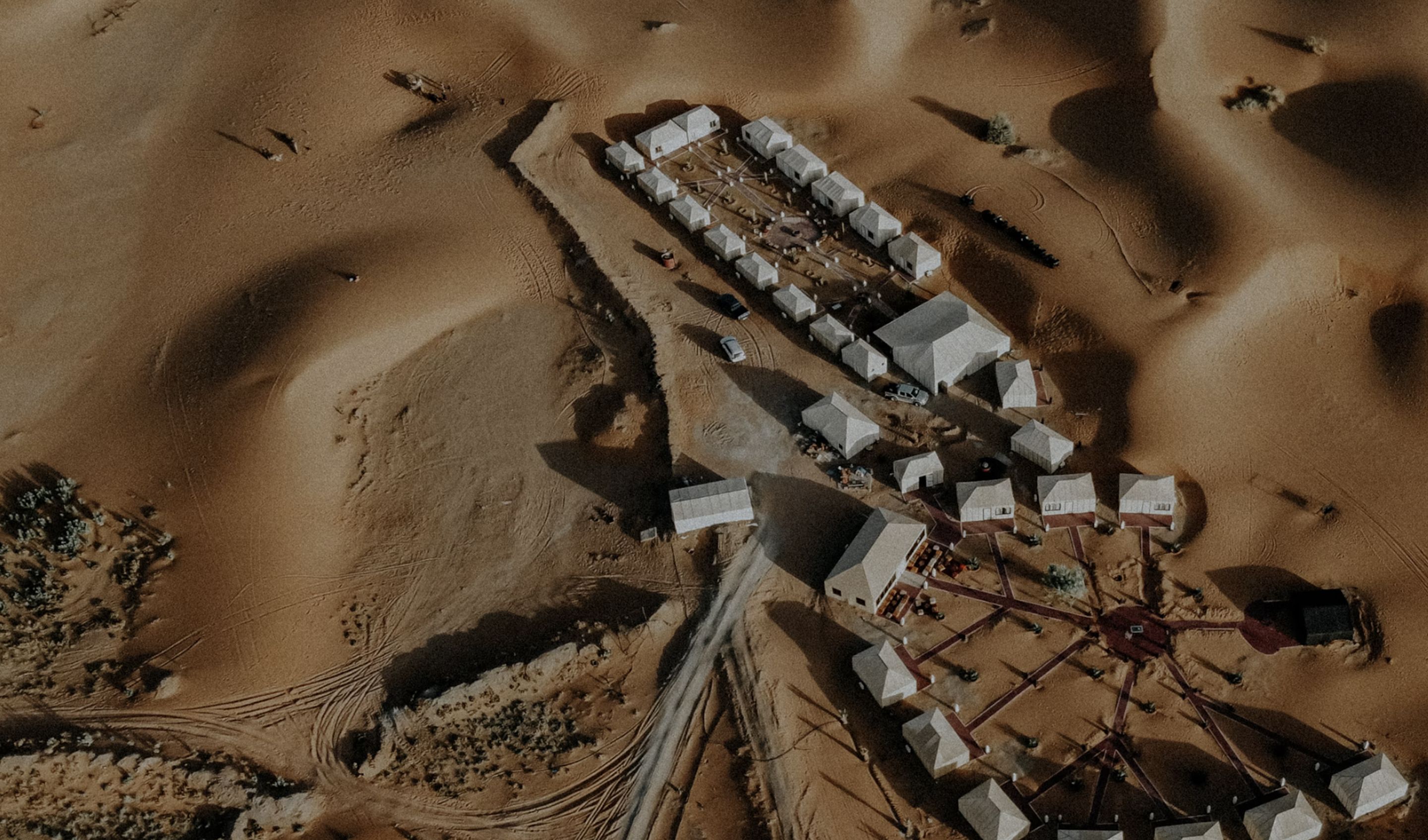 Aerial view of a camp of white buildings among desert dunes
