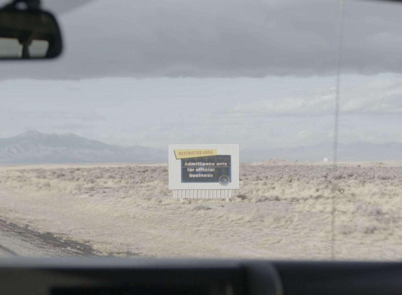 A restricted-area sign by the desert road to the site, seen through a windscreen