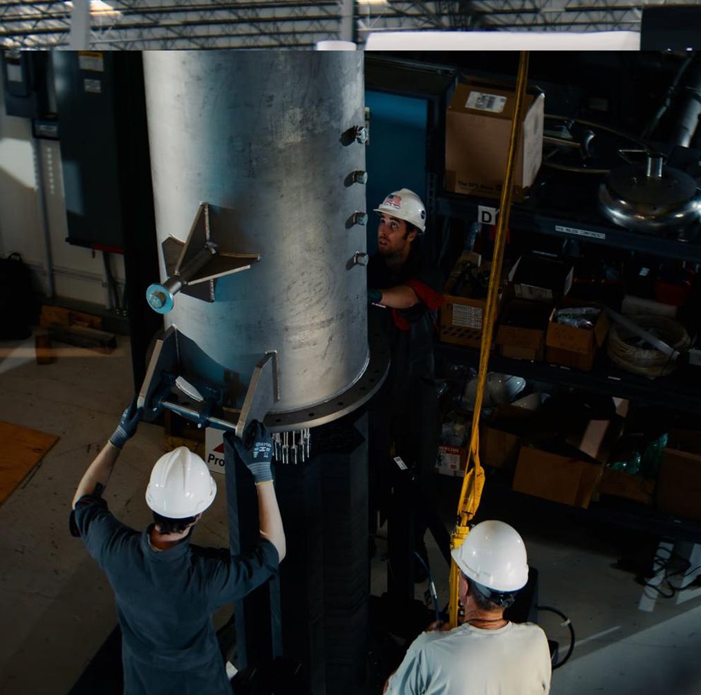 Two engineers in hard hats lifting a heat pipe assembly into place