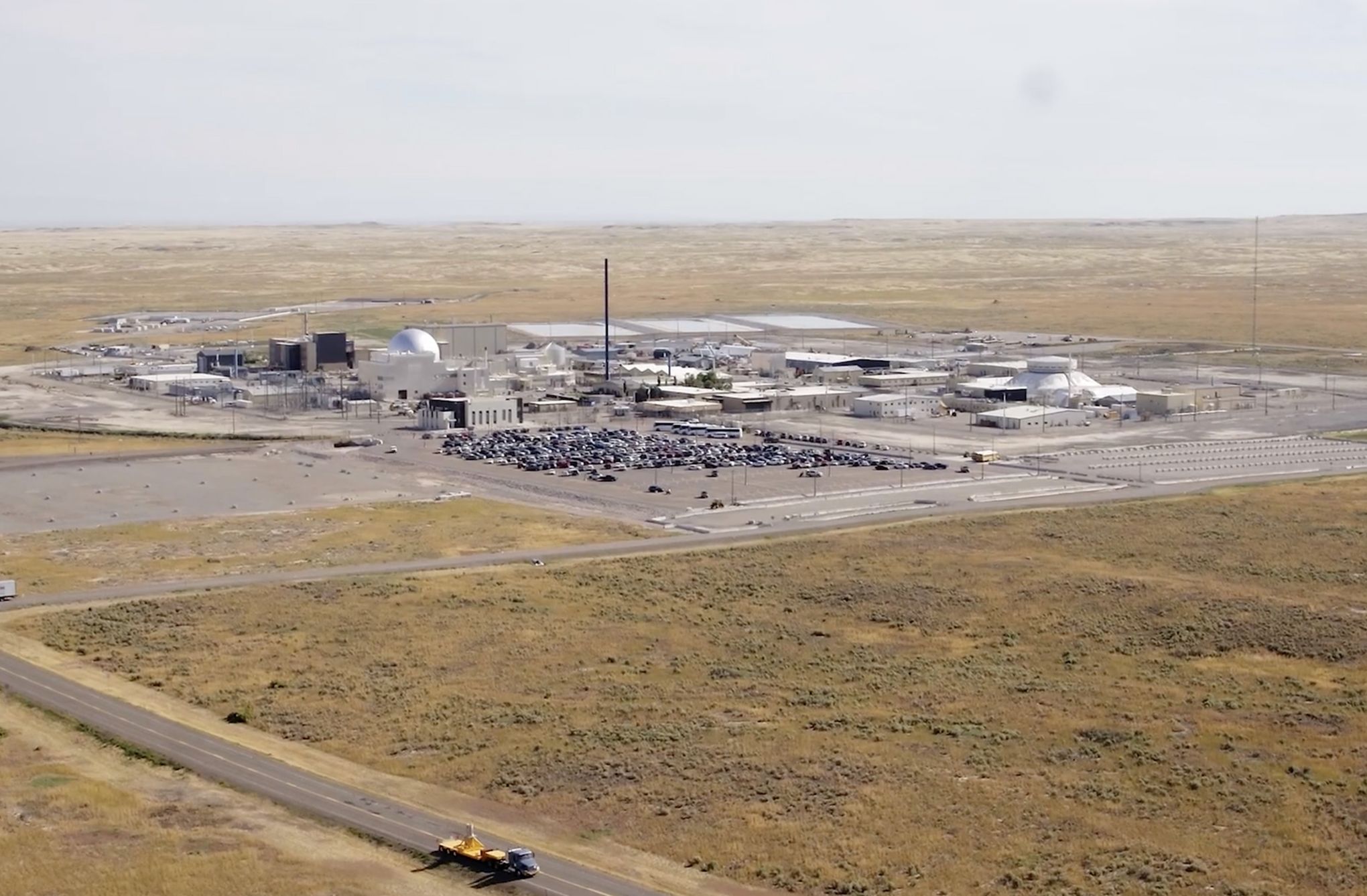 Aerial view of a test site on the plains, a crowd gathered among the low buildings
