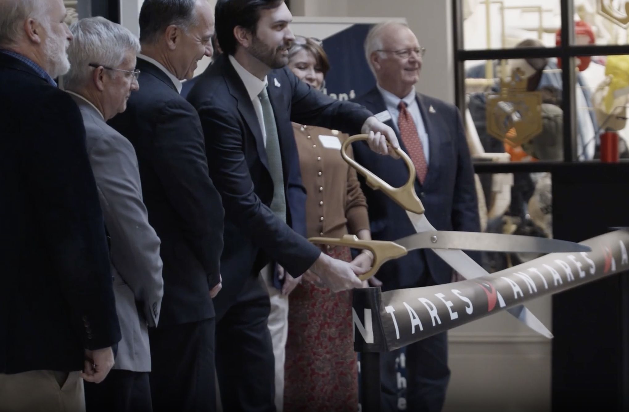 Officials in suits cutting a ribbon with oversized scissors at the Antares opening